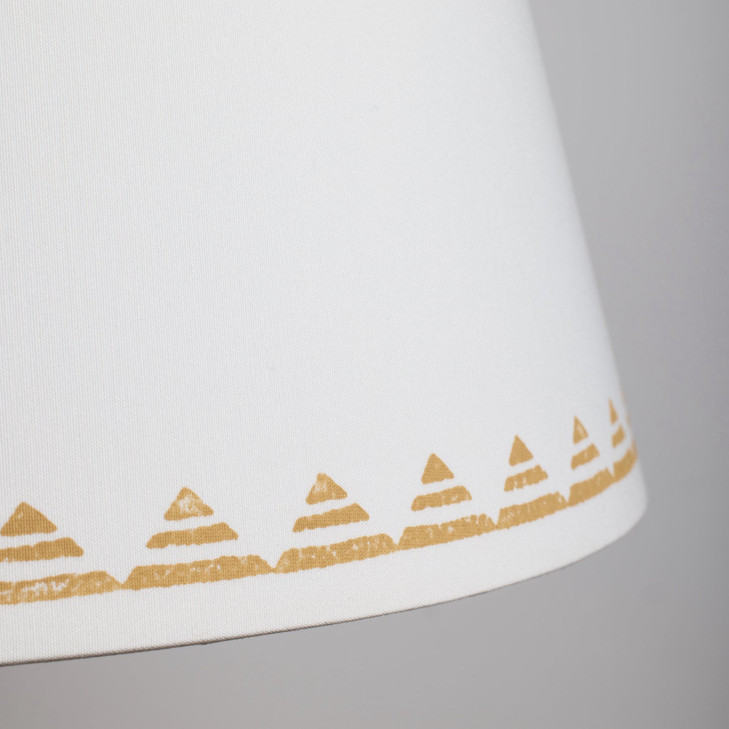 Close-up of a cream empire lampshade with a yellow triangle pattern along the bottom edge. The geometric lampshade features hand-printed lines inside each triangle, creating a modern yet neutral lampshade design.