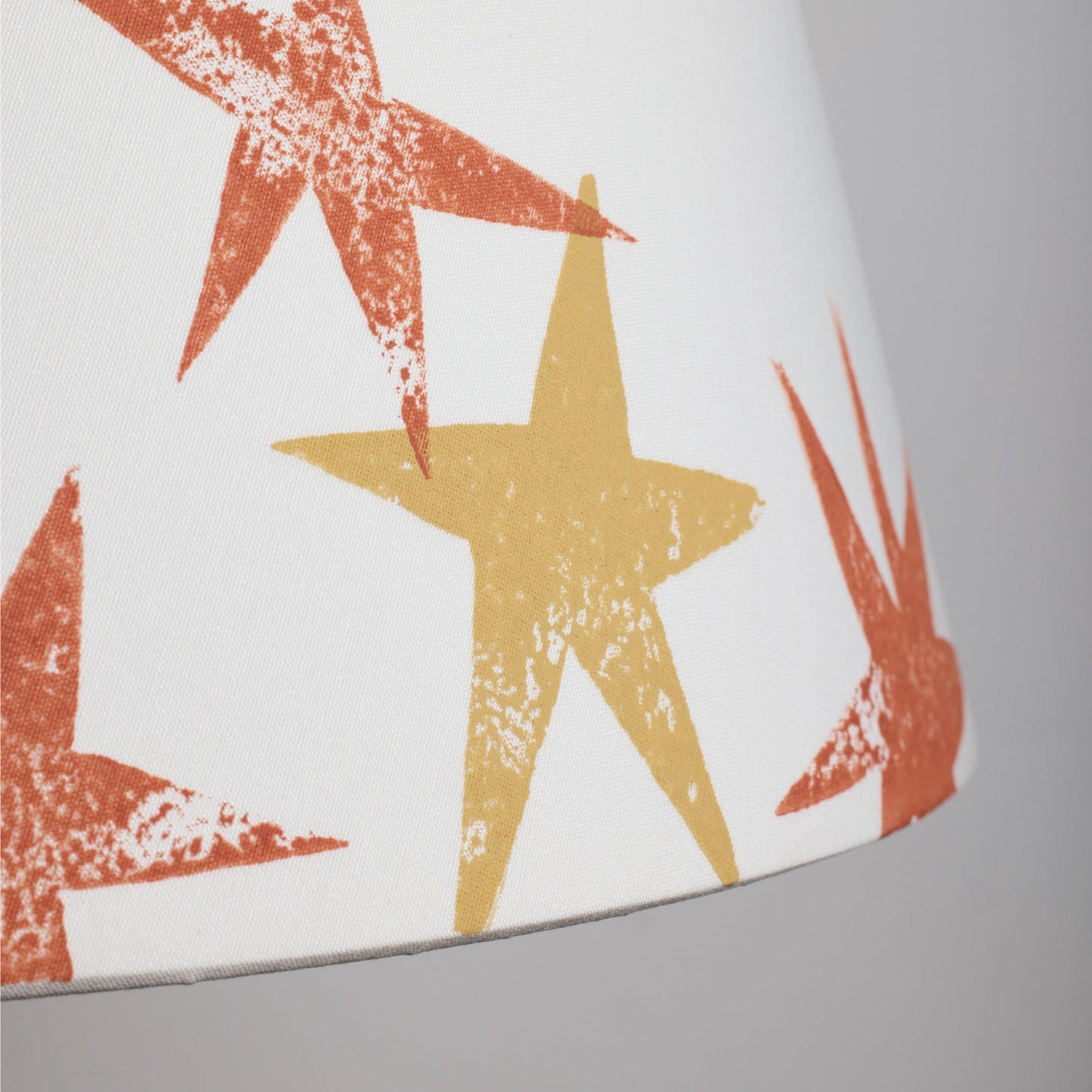 Close-up of a cream lampshade fabric showing bright orange lampshade and yellow lampshade star prints, highlighting the bold, playful design of this star lampshade.