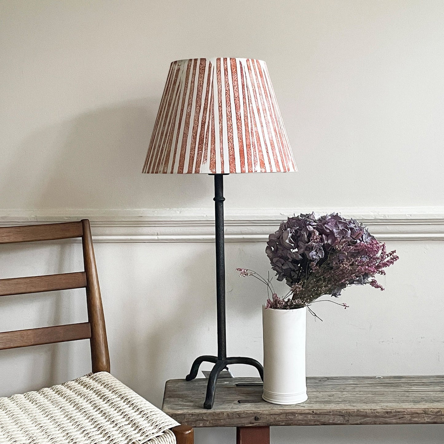 Empire light shade in a bold stripe design with orange and cream tones, styled on a tall metal lamp beside a modern chair. A colourful lampshade for modern interiors, perfect for striped lampshades UK collections.