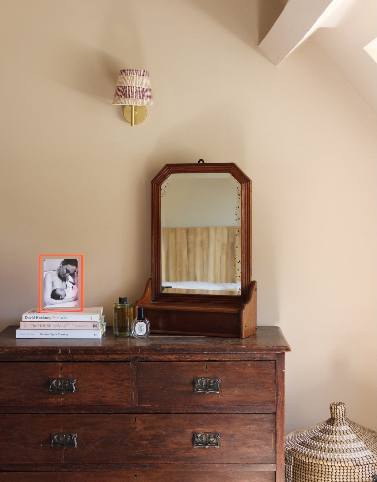 Burgundy and pink striped lampshade mounted on a brass wall fitting, bold lampshade styled above a vintage wooden chest of drawers with framed artwork and decorative accents.