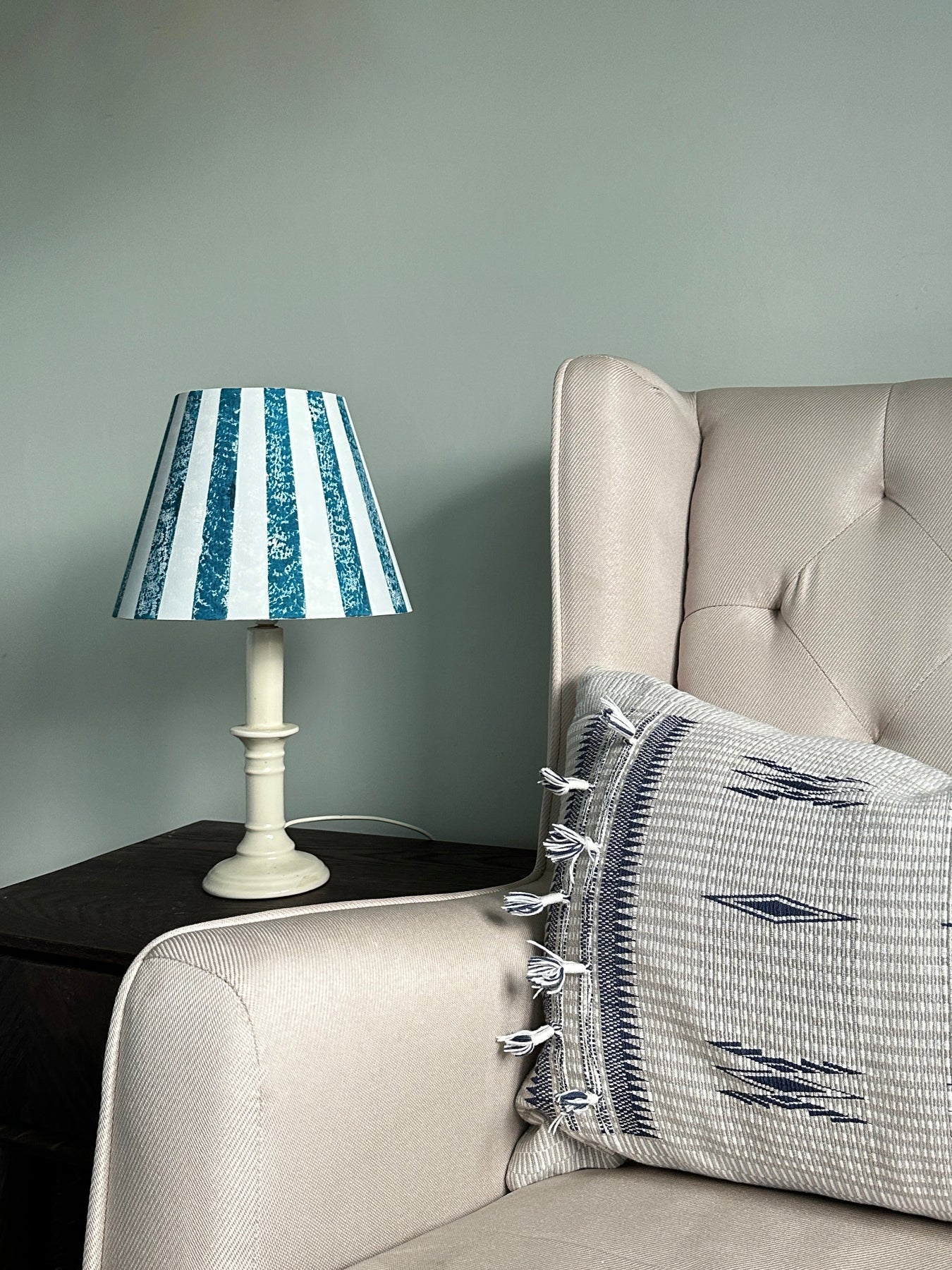 Bold blue stripe lampshade styled on a white table lamp next to an armchair. A bold and colourful lampshade for table lamps, ideal for striped lighting in modern homes.