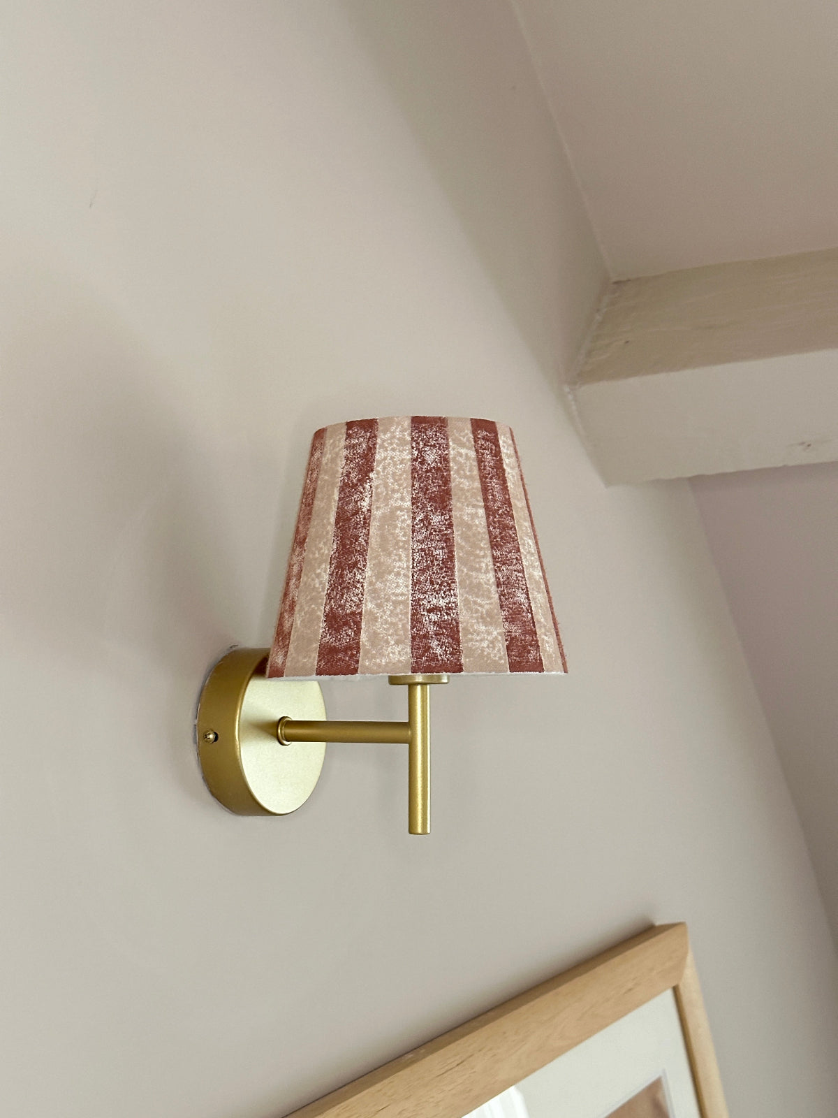 Bold stripe lampshade in burgundy and pink, styled as a wall light shade on a brass sconce. A striped lampshade design perfect for striped lighting and empire light shades in UK interiors.