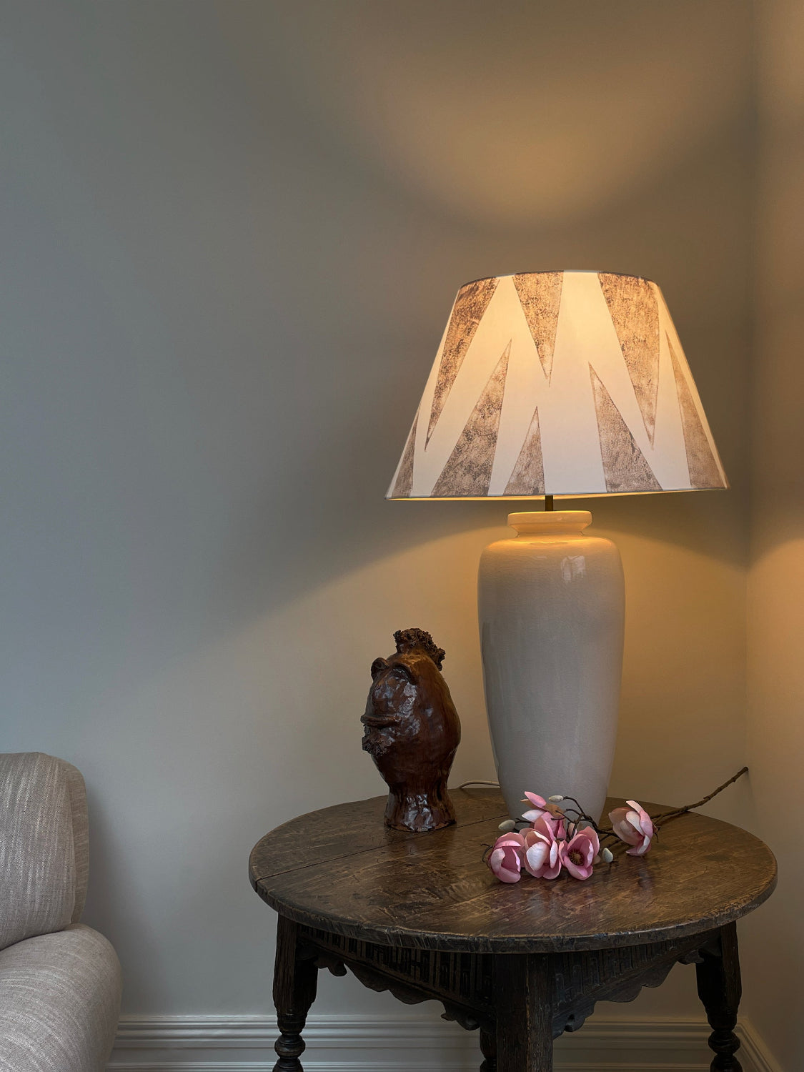 Large empire light shade with tiger tooth triangle pattern in warm pink on cream cotton, placed on a ceramic lamp in a cosy living room. A bold and neutral lampshade design, perfect for geometric lighting.