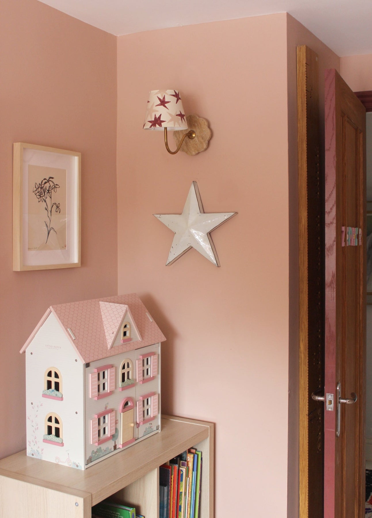 A wall-mounted empire light shade with bold red and pink stars, adding a playful accent to a girl's bedroom decor. The pink girls bedroom has a dolls house, books flower art. A star lampshade and colourful lampshade ideal for kids lampshade styling.