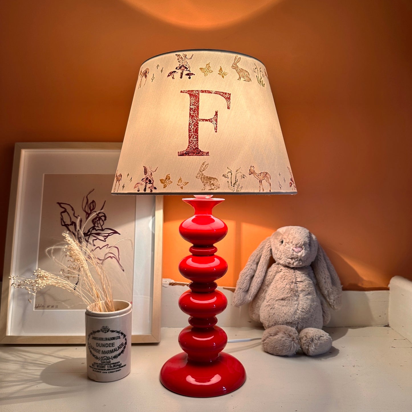 Empire lampshade for kids bedroom with woodland animals and personalised initial, lit to show warm kids lighting. A colourful lampshade and personalised kids gift perfect for bedtime reading.