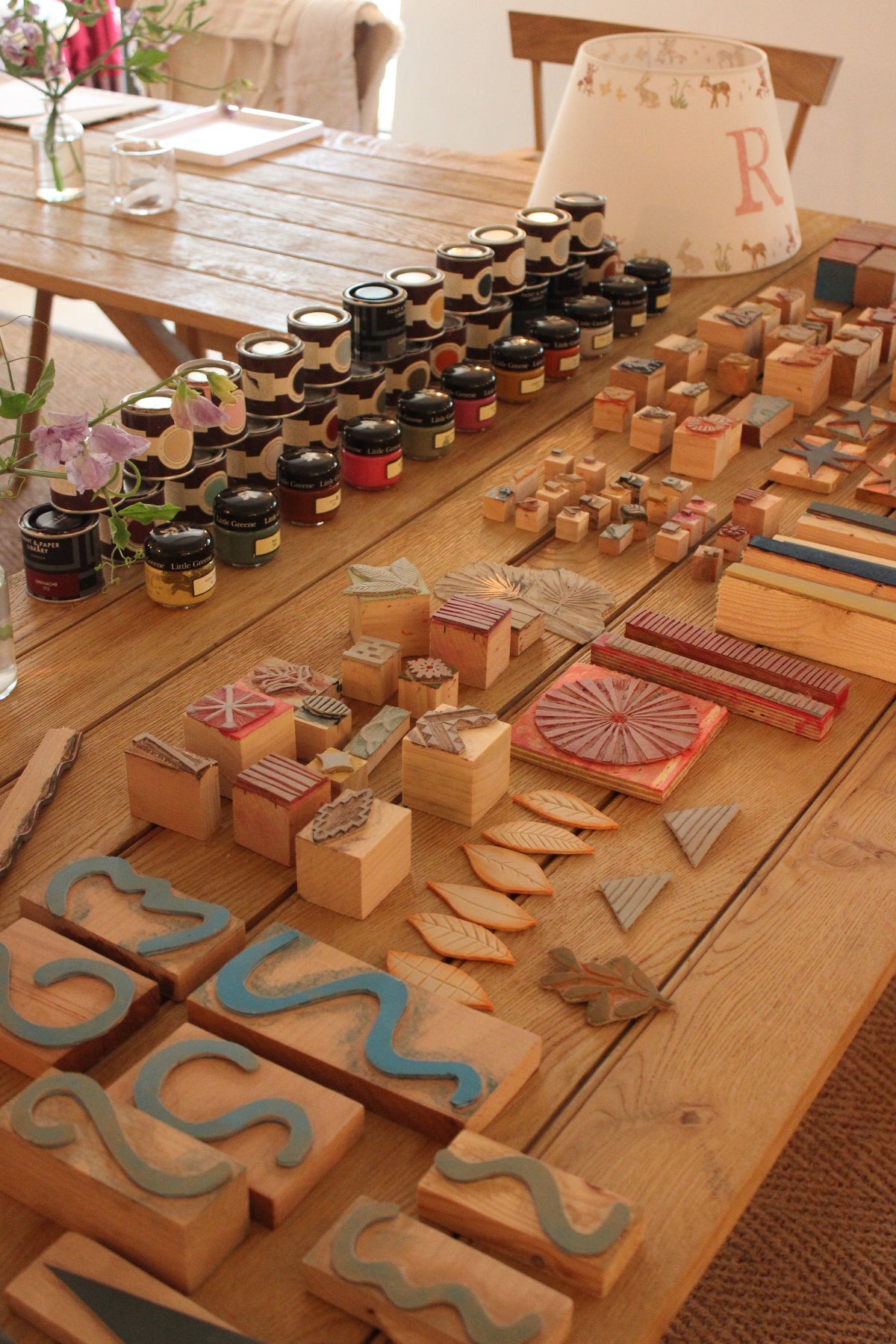 Studio Zef hand printing lampshade workshop at The Bell in Charlbury, showing wooden printing blocks, paint pots, and a partially decorated handmade lampshade, offering an artisanal craft experience in bespoke lampshade design.