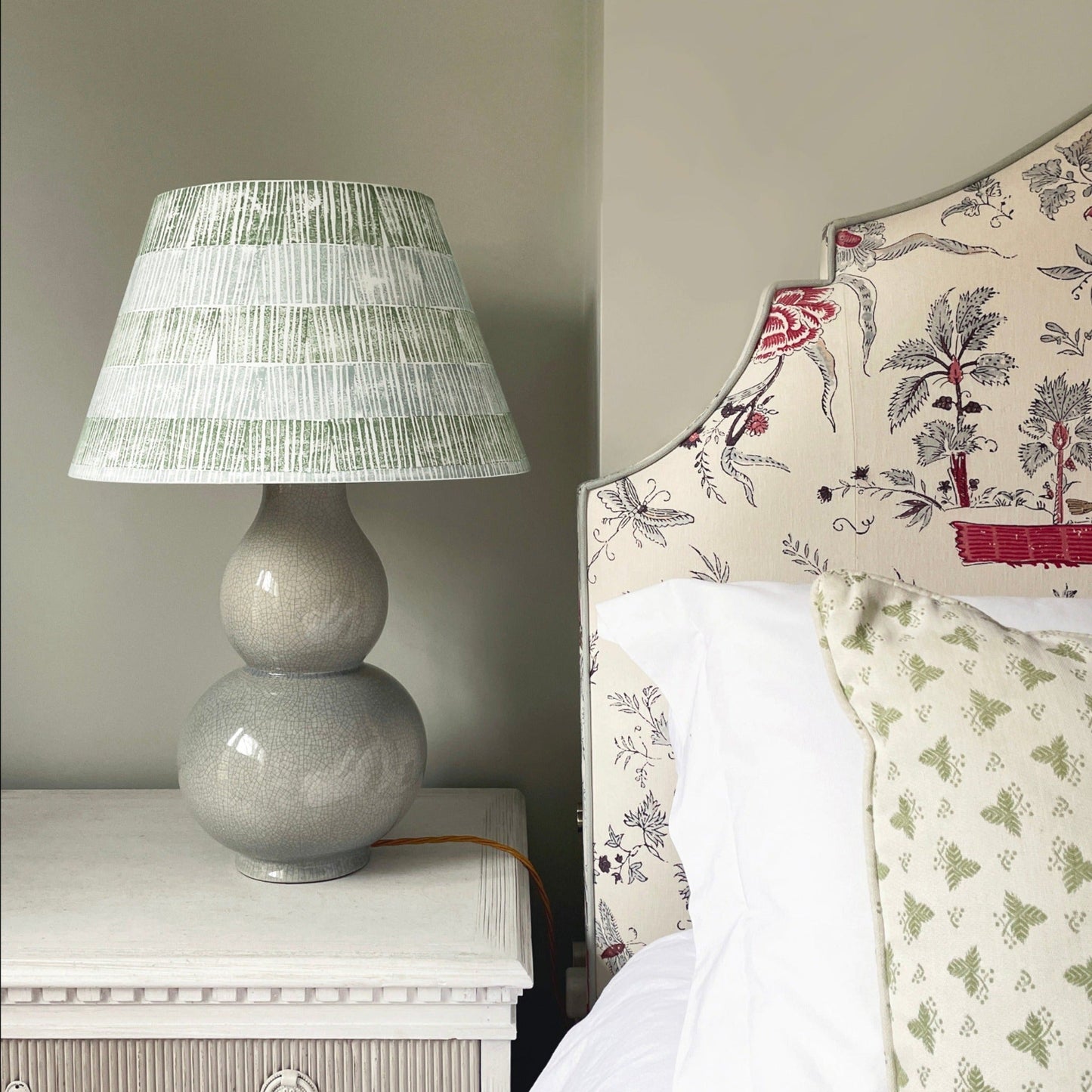 Empire lampshade with green and blue stripes, bold stripe design paired with a ceramic double-gourd lamp base beside a patterned upholstered headboard.