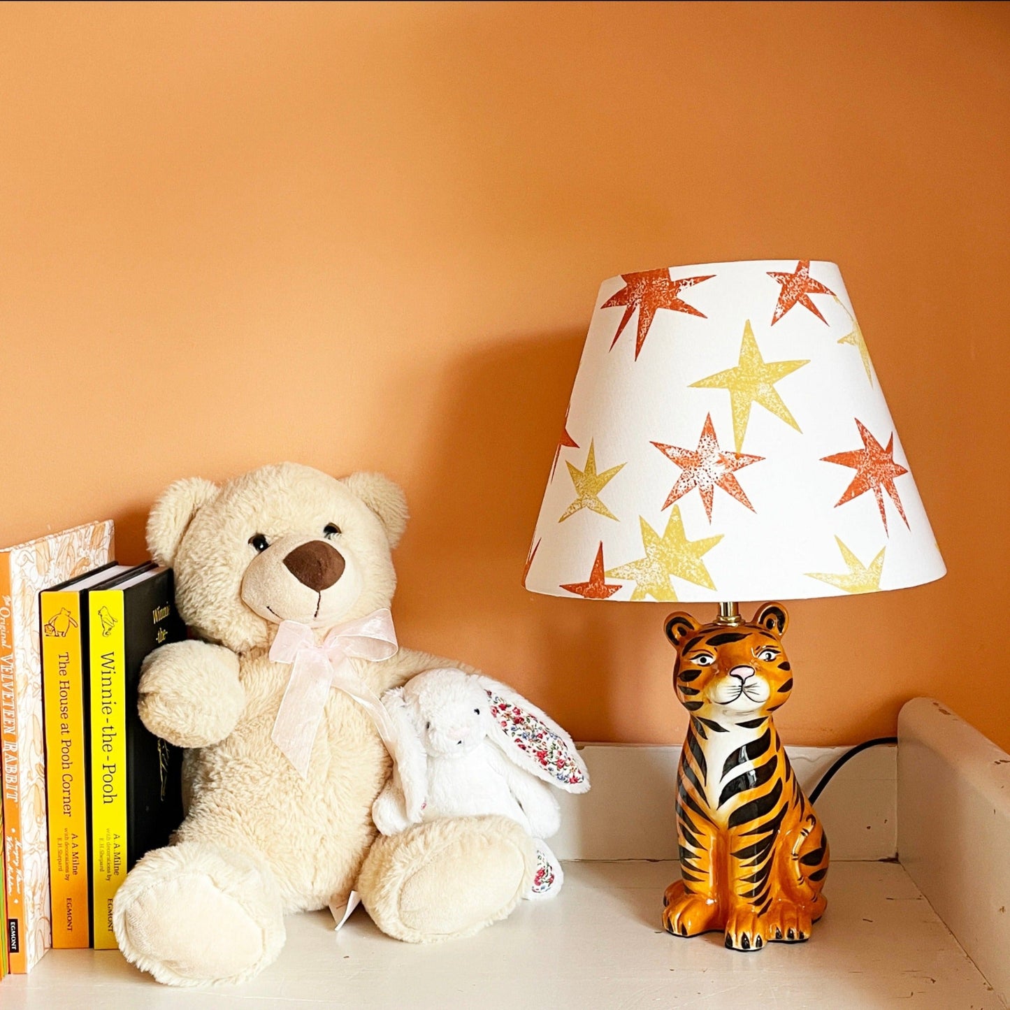 A cream lampshade decorated with bright orange and yellow star patterns, styled in a kids bedroom on a tiger lamp base. A fun empire lampshade and kids bedroom decor piece that adds warmth and character.