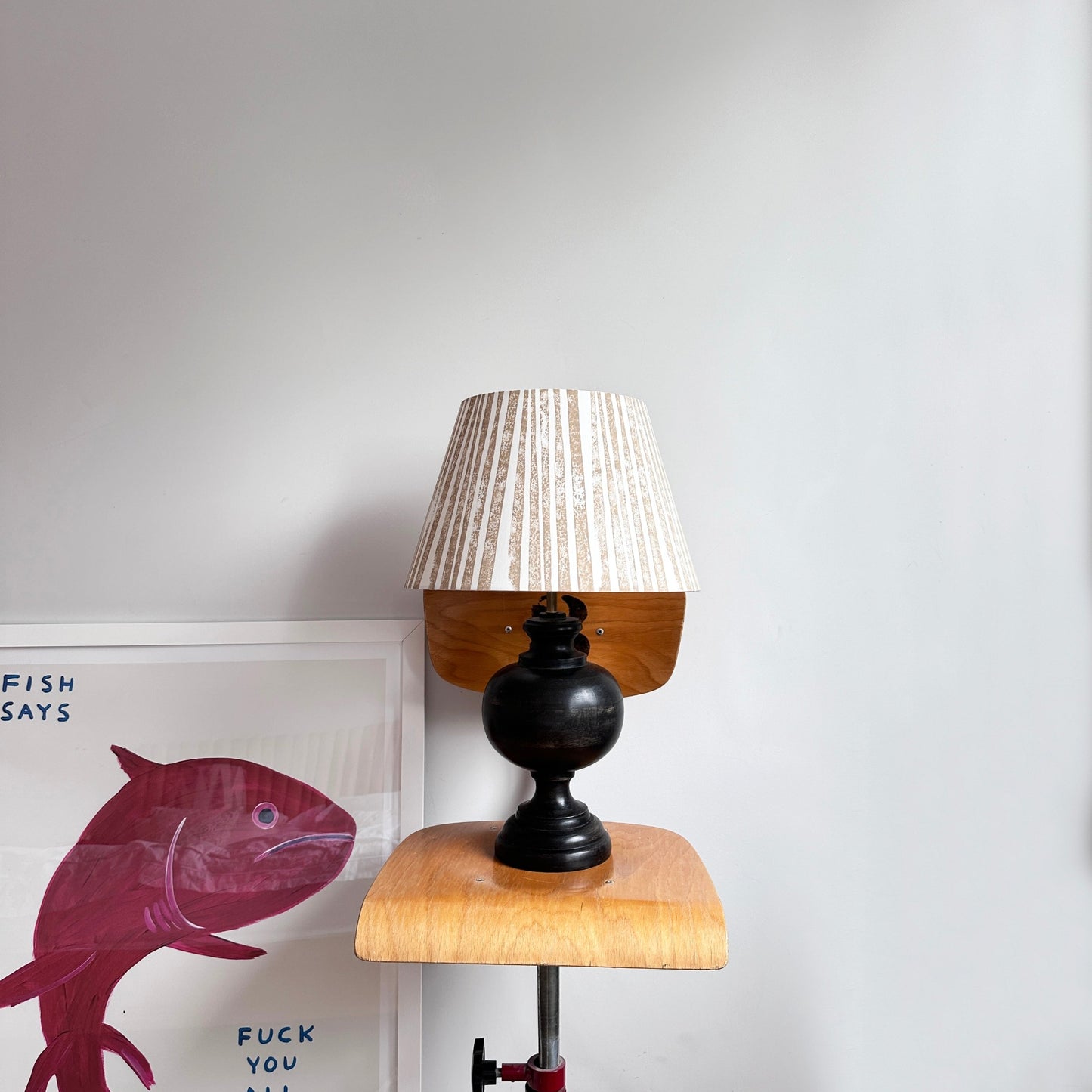 Striped brown lampshade on black lamp next to David Shrigley print