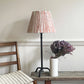 Empire light shade in a bold stripe design with orange and cream tones, styled on a tall metal lamp beside a modern chair. A colourful lampshade for modern interiors, perfect for striped lampshades UK collections.