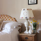 A cosy children's bedroom with a rustic wooden nightstand featuring a personalised lampshade with the letter "C" and a countryside pattern. A plush goose, daffodils, and white bedding add charm. Neutral empire light shade with pretty animal details, ideal for kids bedroom design and personalised kids gift.