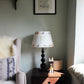 Safari lampshade with letter F, styled on side table in bright boys bedroom. Handmade safari lampshade for kids bedroom, personalised with letter F. Colourful empire light shade with safari animals, a green lampshade option for boys lampshade or kids bedroom design. The lamp is on a dark blue lamp base next to a cream arm chair with blue cushion and sheep skin. 