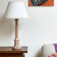 Styled sitting room scene with a cream empire lampshade featuring a yellow triangle border. The geometric lampshade sits on a carved wooden lamp base beside a neutral-toned sofa and bold artwork, blending modern design with cosy decor.