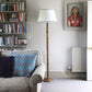 Living room interior full of sofa, bookshelf and portrait art, has a tall floor lamp fitted with a cream empire lampshade with a blue triangle pattern. This neutral lampshade with geometric detail adds a subtle colourful accent to the space.