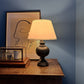 Romantic evening setting with a glowing cream empire lampshade featuring a lined triangle border in dark ink blue. The geometric lampshade casts a warm light, styled on a dark wooden lamp base against a deep blue wall.