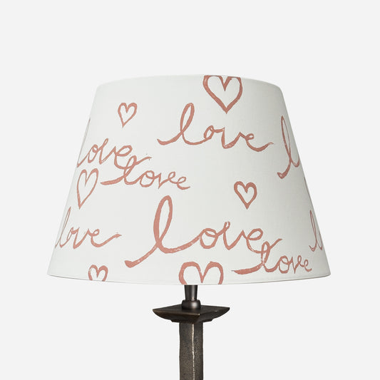 Cut out image of a handmade empire lampshade with a block-printed design featuring the handwritten word "love" and heart motifs. The cream card lampshade has a modern, romantic aesthetic.