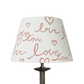 Handmade empire-shaped lampshade with a block-printed design featuring the handwritten word "love" and heart motifs. The lampshade is made from cream cotton and has a modern, romantic aesthetic.