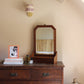 Burgundy and pink striped lampshade mounted on a brass wall fitting, bold lampshade styled above a vintage wooden chest of drawers with framed artwork and decorative accents.