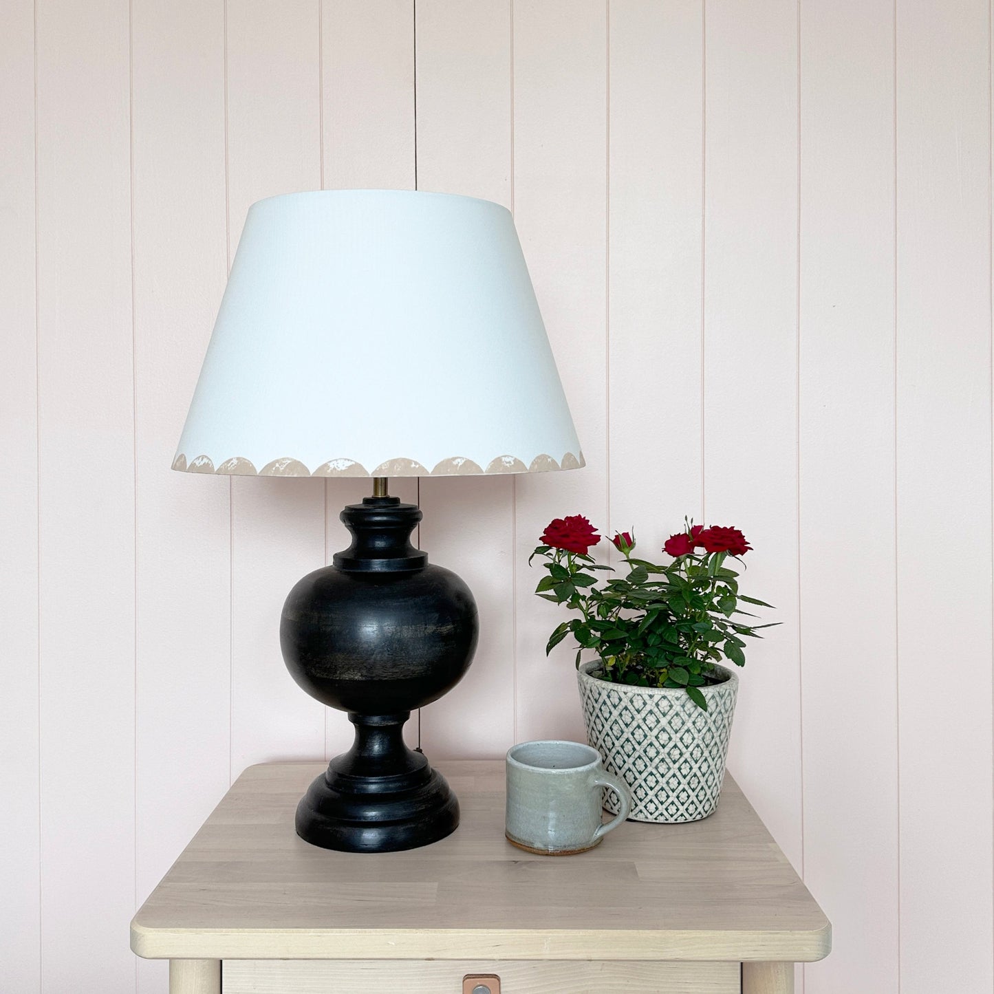 Pink scallop lampshade on black lamp next to flowers