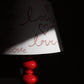 A close up image of an empire shaped lampshade with the hand written word 'Love' hand printed on to it with heart motifs. The lighting is natural but at stark contrast highlighting the word Love on the lampshade. 