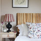 Empire lampshade with bold burgundy and pink stripes, styled on a black table lamp beside a bed with a wooden Tikamoon headboard. A colourful lampshade and classic striped lampshade for bedrooms.