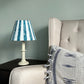 Bold blue stripe lampshade styled on a white table lamp next to an armchair. A bold and colourful lampshade for table lamps, ideal for striped lighting in modern homes.