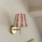 Bold stripe lampshade in burgundy and pink, styled as a wall light shade on a brass sconce. A striped lampshade design perfect for striped lighting and empire light shades in UK interiors.