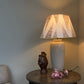 Large empire light shade with tiger tooth triangle pattern in warm pink on cream cotton, placed on a ceramic lamp in a cosy living room. A bold and neutral lampshade design, perfect for geometric lighting.