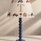 A personalized farm-themed table lamp with a blue beaded stem and a cream fabric shade decorated with colorful tractors, a pig, a goose, and a large gold initial 'T'.