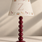A personalized table lamp with a glossy dark red beaded stem and a cream-colored conical shade decorated with a large letter 'Z', rainbows, unicorns, and hearts.