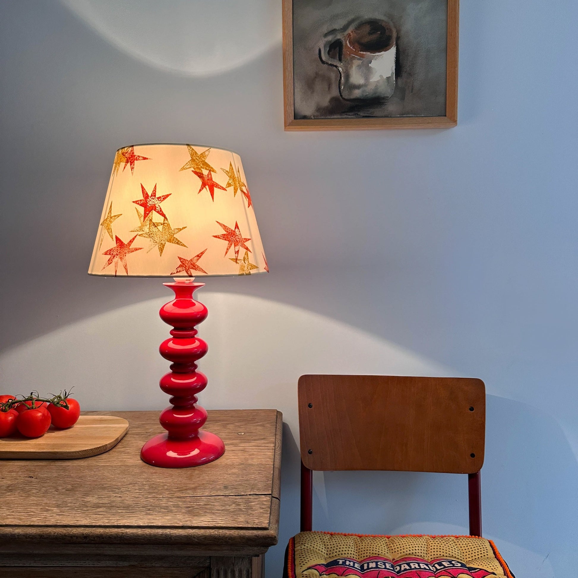 Cream lampshade with orange and yellow stars on a red lamp with light on