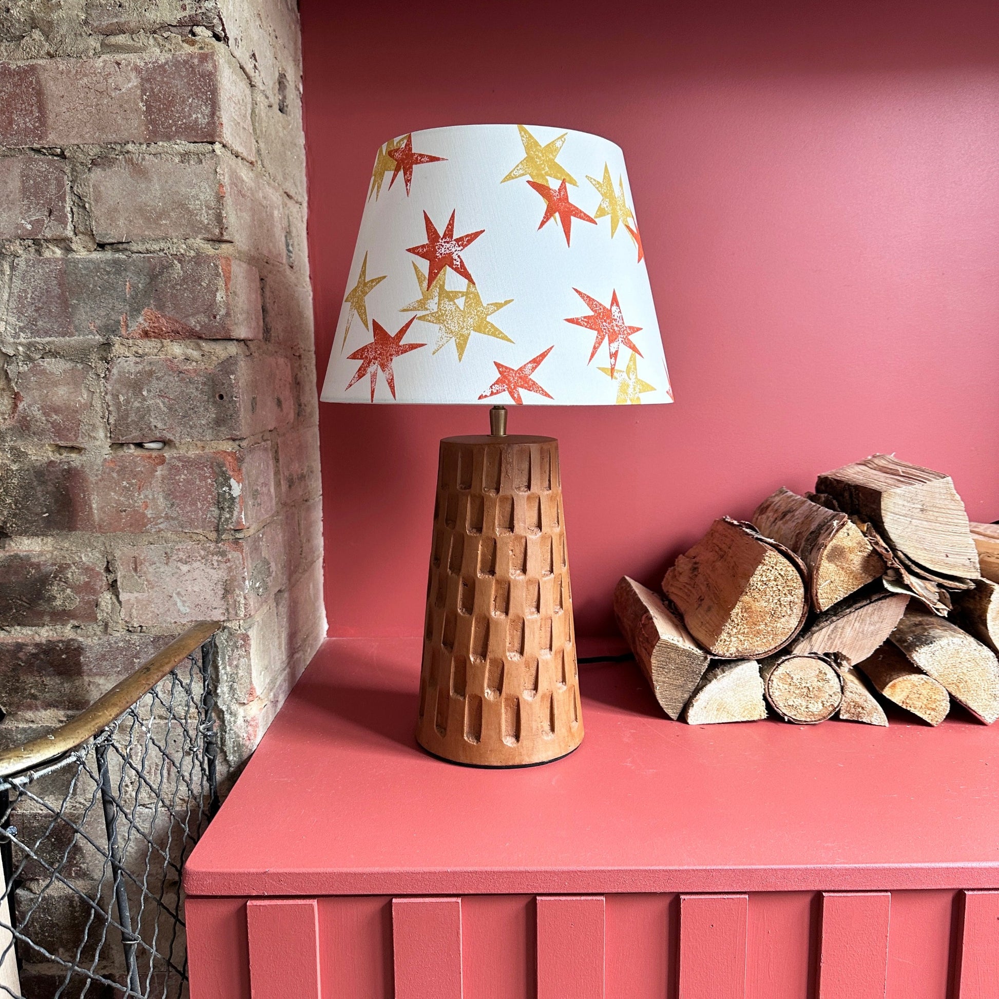 Cream lampshade with orange and yellow stars on brown lamp next to fire place