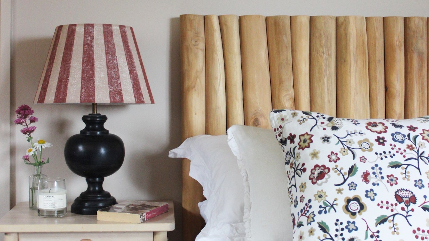 Studio Zef hand-printed linen lampshade with bold red and pink stripes on a black wooden table lamp, styled in a cosy bedroom with wooden headboard, floral cushion, and artisan home décor.