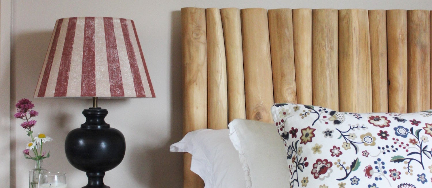 Studio Zef hand-printed linen lampshade with bold red and pink stripes on a black wooden table lamp, styled in a cosy bedroom with wooden headboard, floral cushion, and artisan home décor.