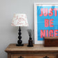 Studio Zef hand-painted lampshade with playful pink ‘Love’ lettering and hearts, styled on a blue table lamp against a modern interior with vintage wooden dresser and bold wall art.