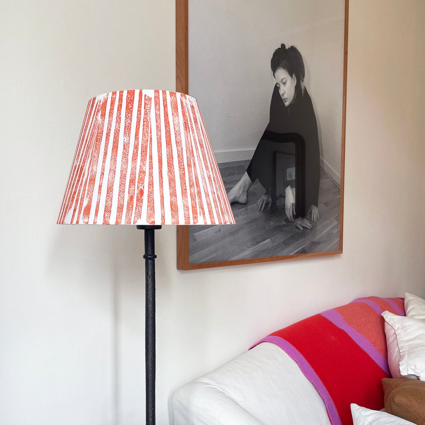 Orange lampshade on iron lamp with sofa and picture behind