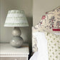 Empire lampshade with green and blue stripes, bold stripe design paired with a ceramic double-gourd lamp base beside a patterned upholstered headboard.