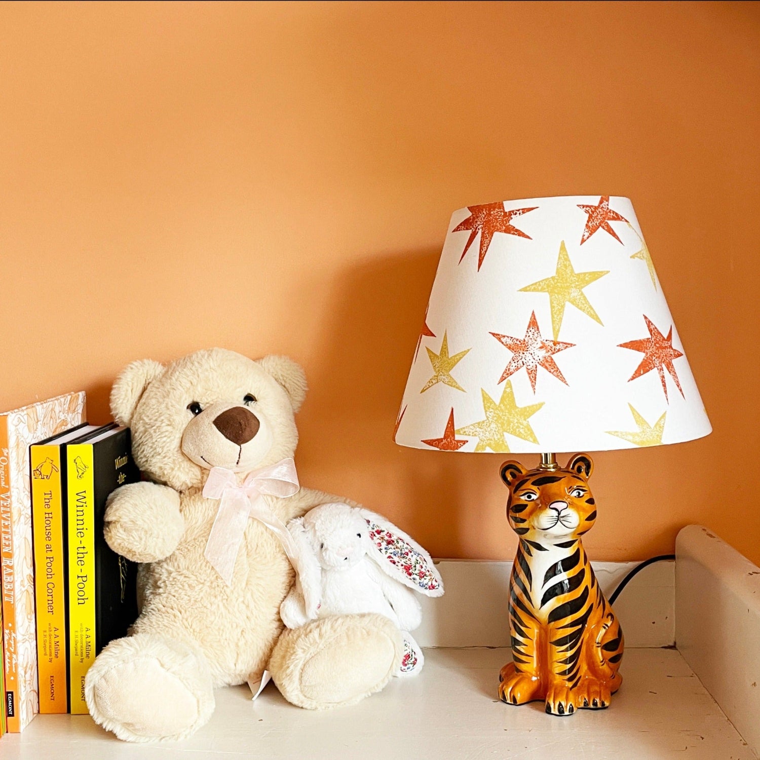 A cream lampshade decorated with bright orange and yellow star patterns, styled in a kids bedroom on a tiger lamp base. A fun empire lampshade and kids bedroom decor piece that adds warmth and character.